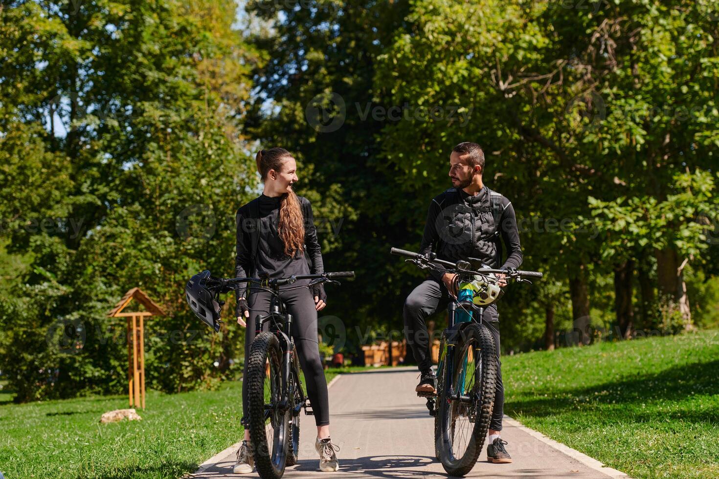 A sweet couple, equipped with bicycles and engrossed in coordinating their journey, checks their GPS mobile and watches while planning scenic routes in the park, seamlessly blending technology and photo