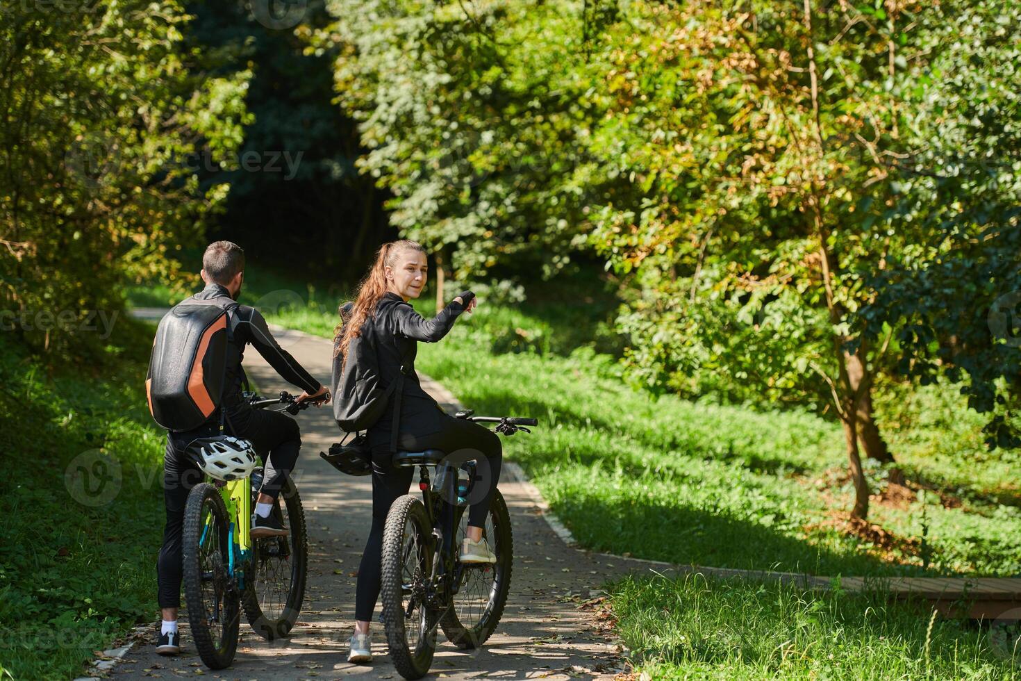 A blissful couple, adorned in professional cycling gear, enjoys a romantic bicycle ride through a park, surrounded by modern natural attractions, radiating love and happiness photo