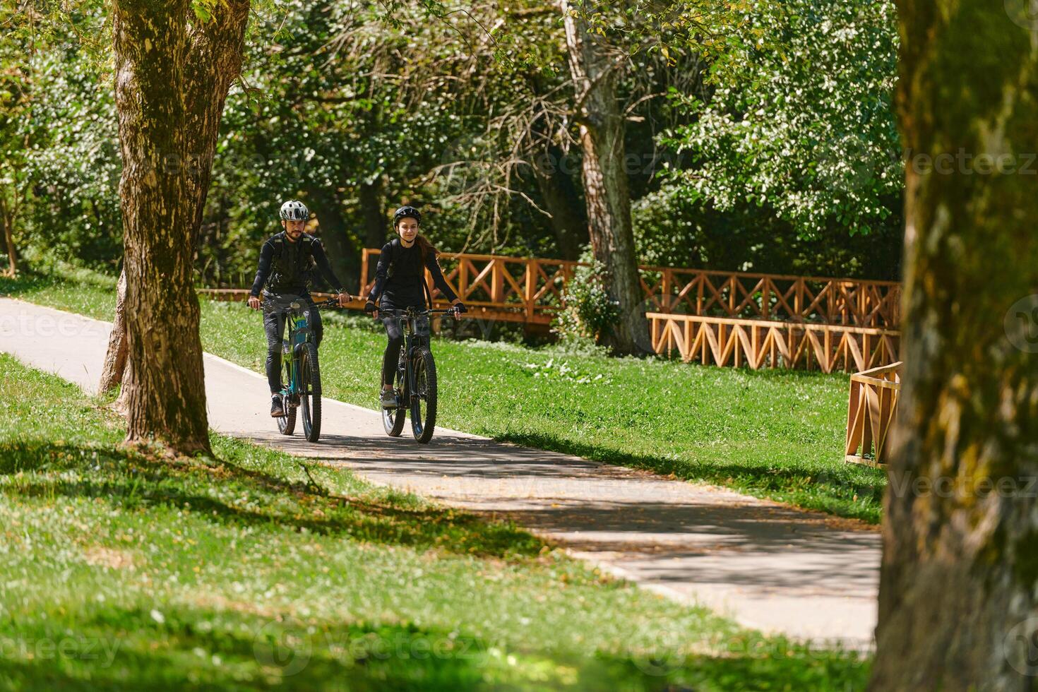 A blissful couple, adorned in professional cycling gear, enjoys a romantic bicycle ride through a park, surrounded by modern natural attractions, radiating love and happiness photo