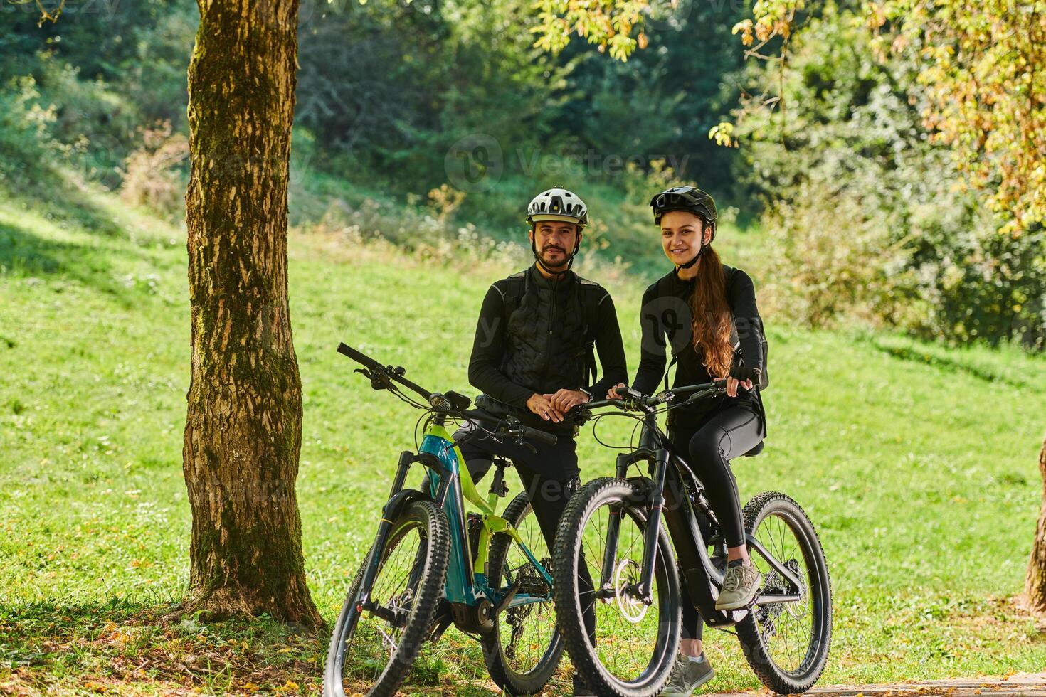A sweet couple, equipped with bicycles and engrossed in coordinating their journey, checks their GPS mobile and watches while planning scenic routes in the park, seamlessly blending technology and photo