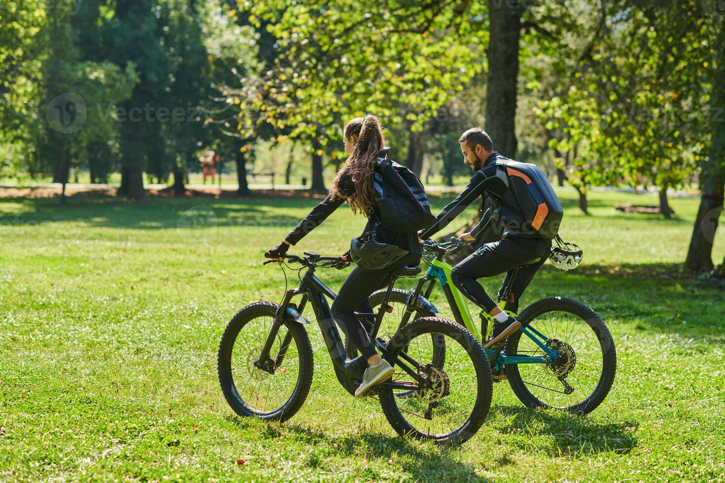A blissful couple, adorned in professional cycling gear, enjoys a romantic bicycle ride through a park, surrounded by modern natural attractions, radiating love and happiness photo
