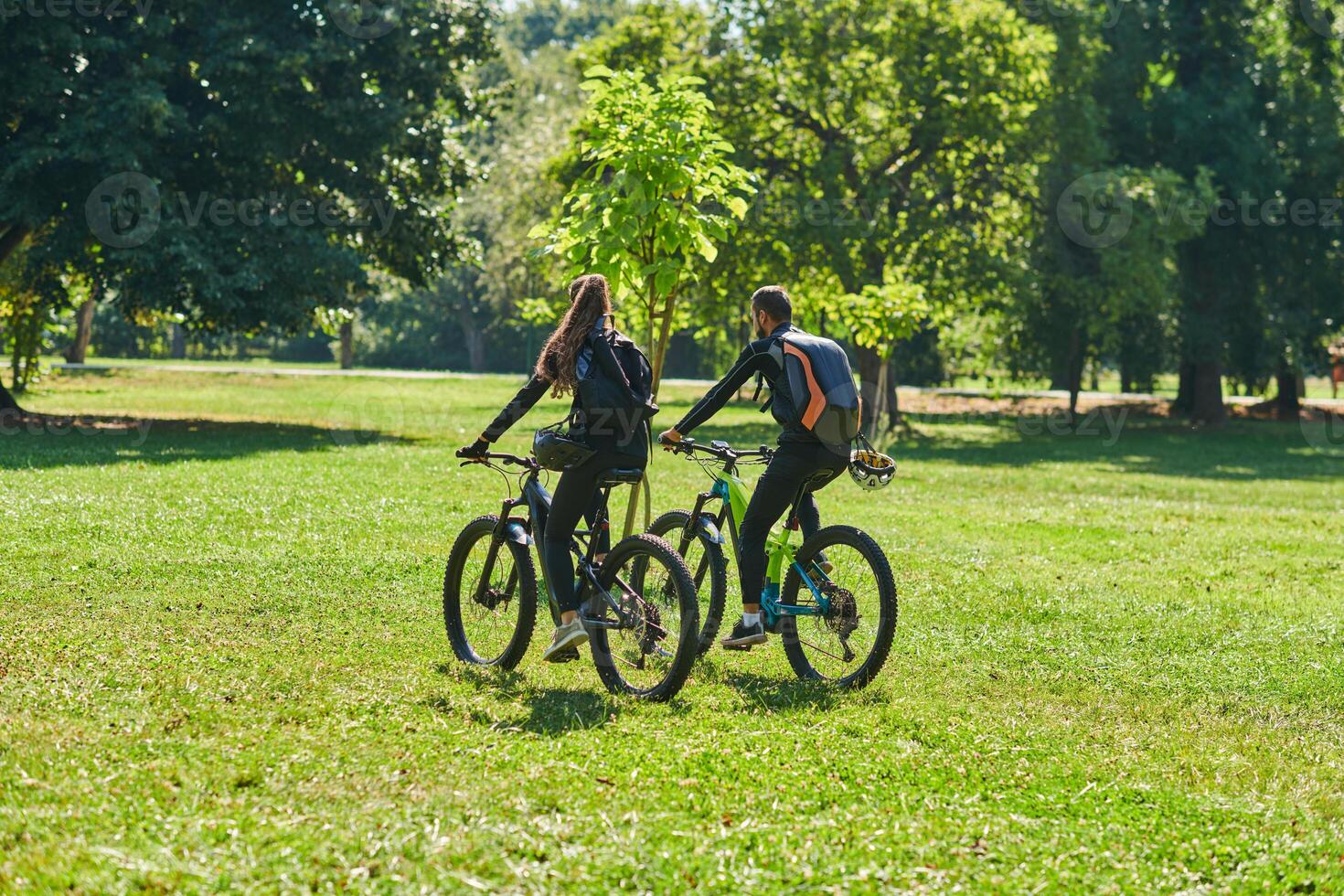 A blissful couple, adorned in professional cycling gear, enjoys a romantic bicycle ride through a park, surrounded by modern natural attractions, radiating love and happiness photo