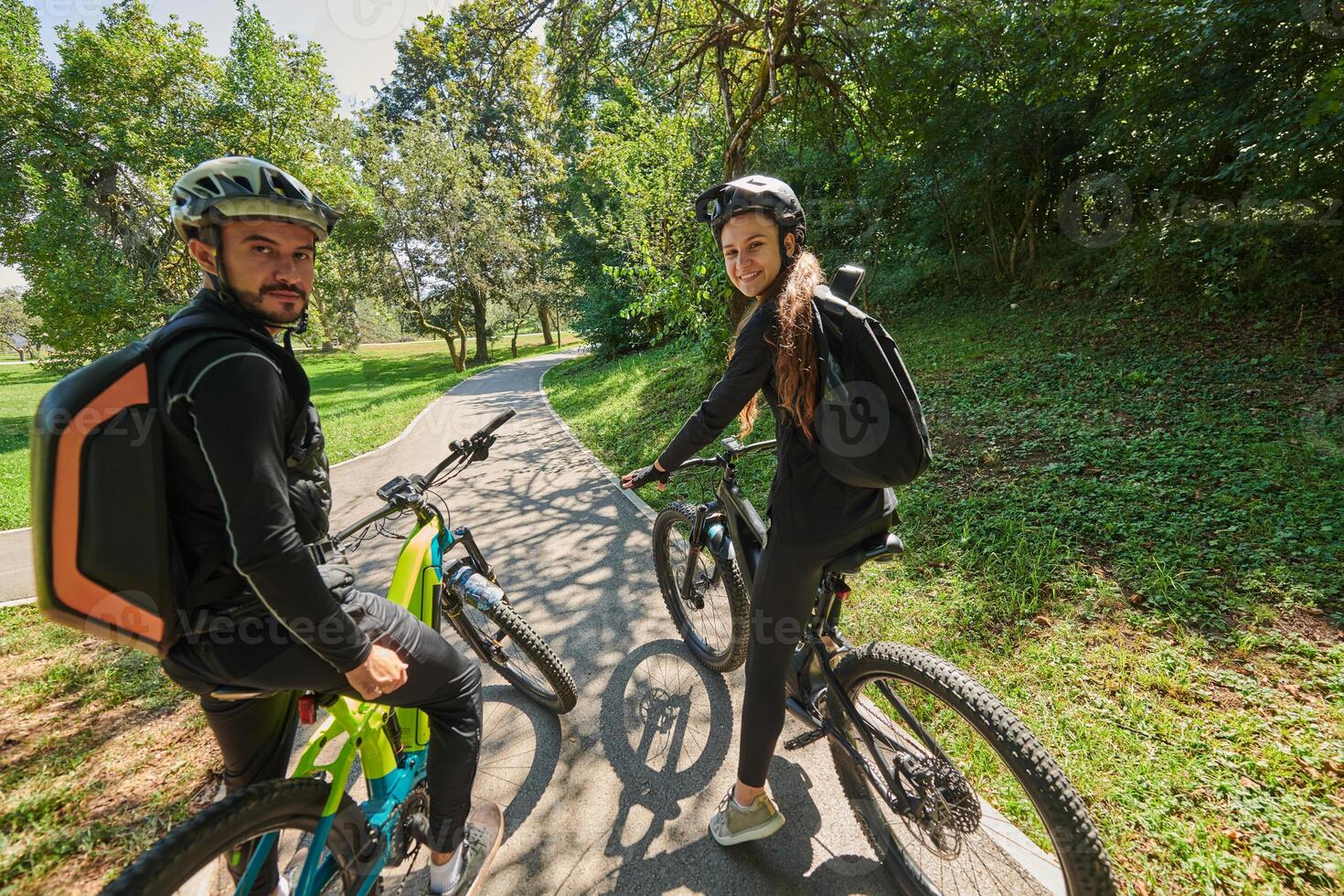 A sweet couple, adorned in cycling gear, rides their bicycles, their hands interlocked in a romantic embrace, capturing the essence of love, adventure, and joy on a sunlit path photo