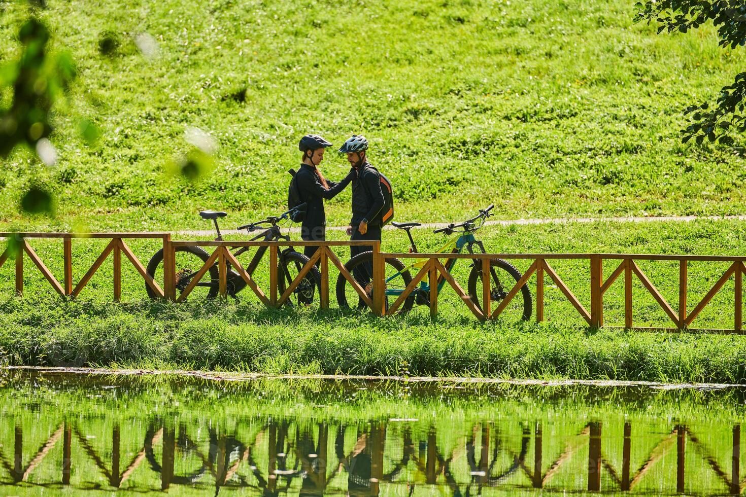 A blissful couple, adorned in professional cycling gear, enjoys a romantic bicycle ride through a park, surrounded by modern natural attractions, radiating love and happiness photo