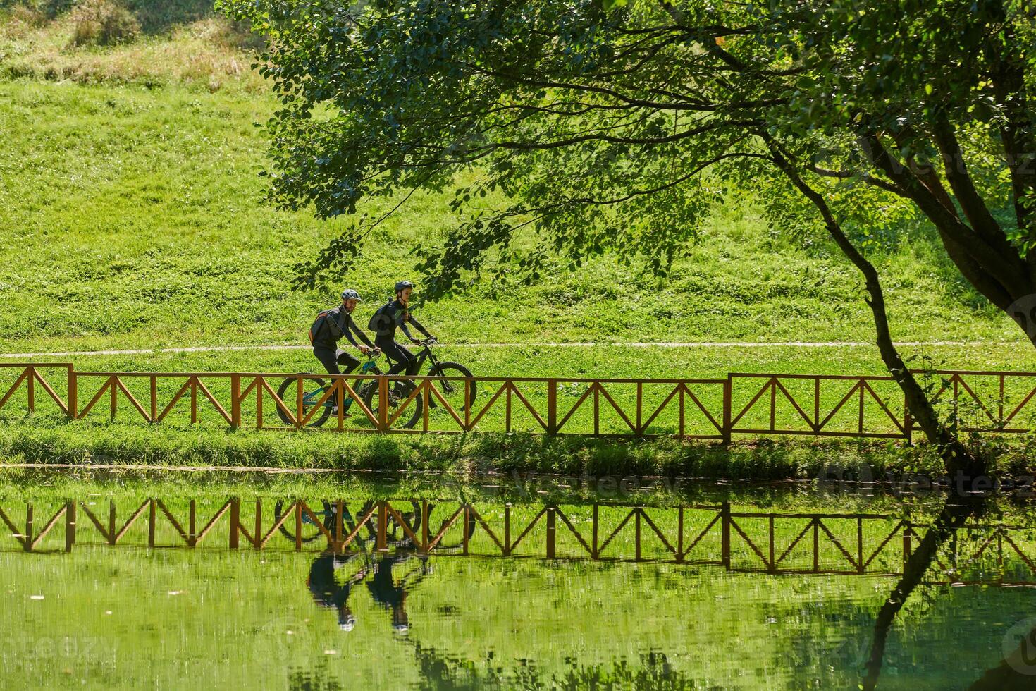A blissful couple, adorned in professional cycling gear, enjoys a romantic bicycle ride through a park, surrounded by modern natural attractions, radiating love and happiness photo