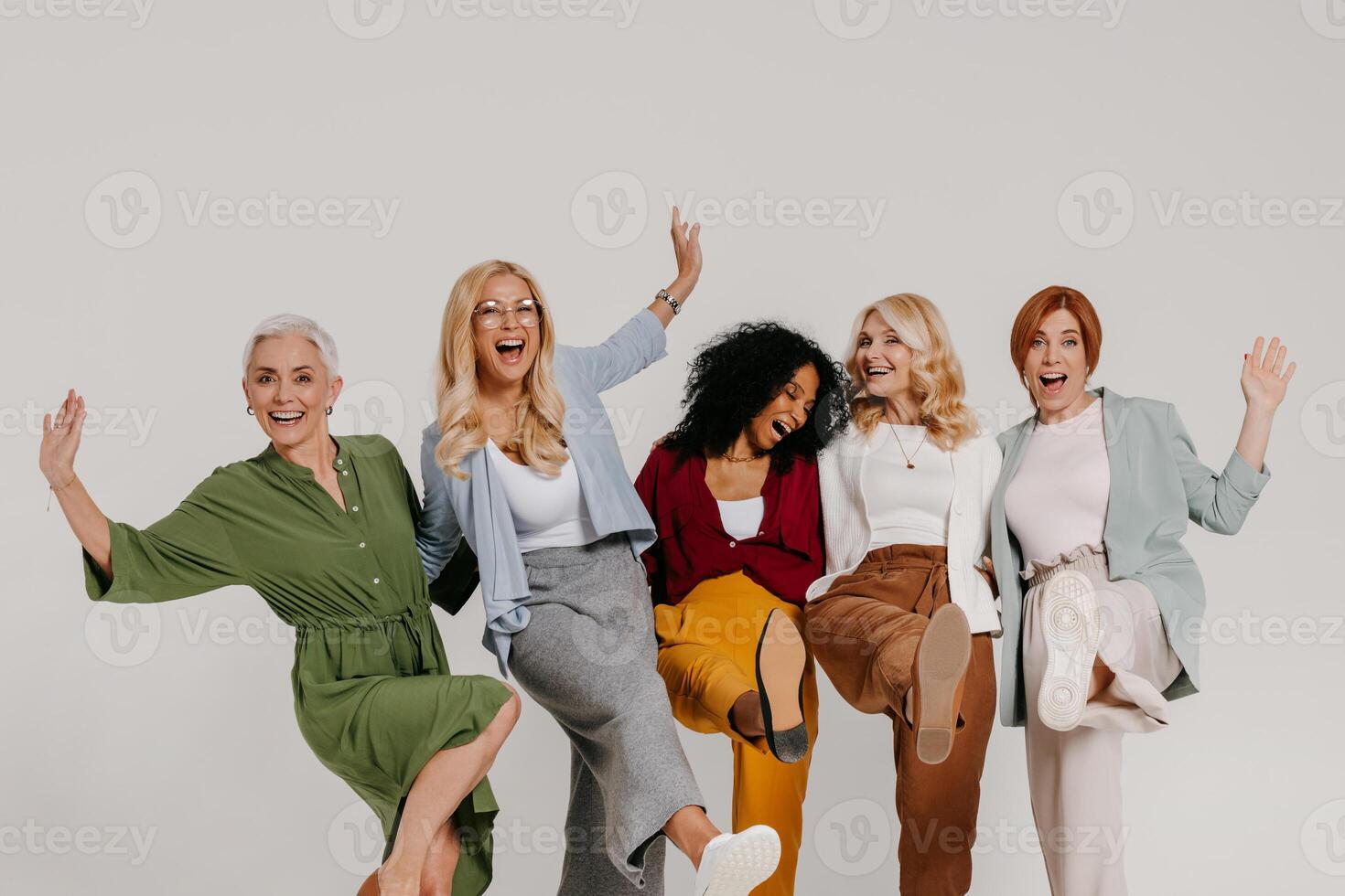 Multi-ethnic group of playful mature women embracing and dancing against grey background photo