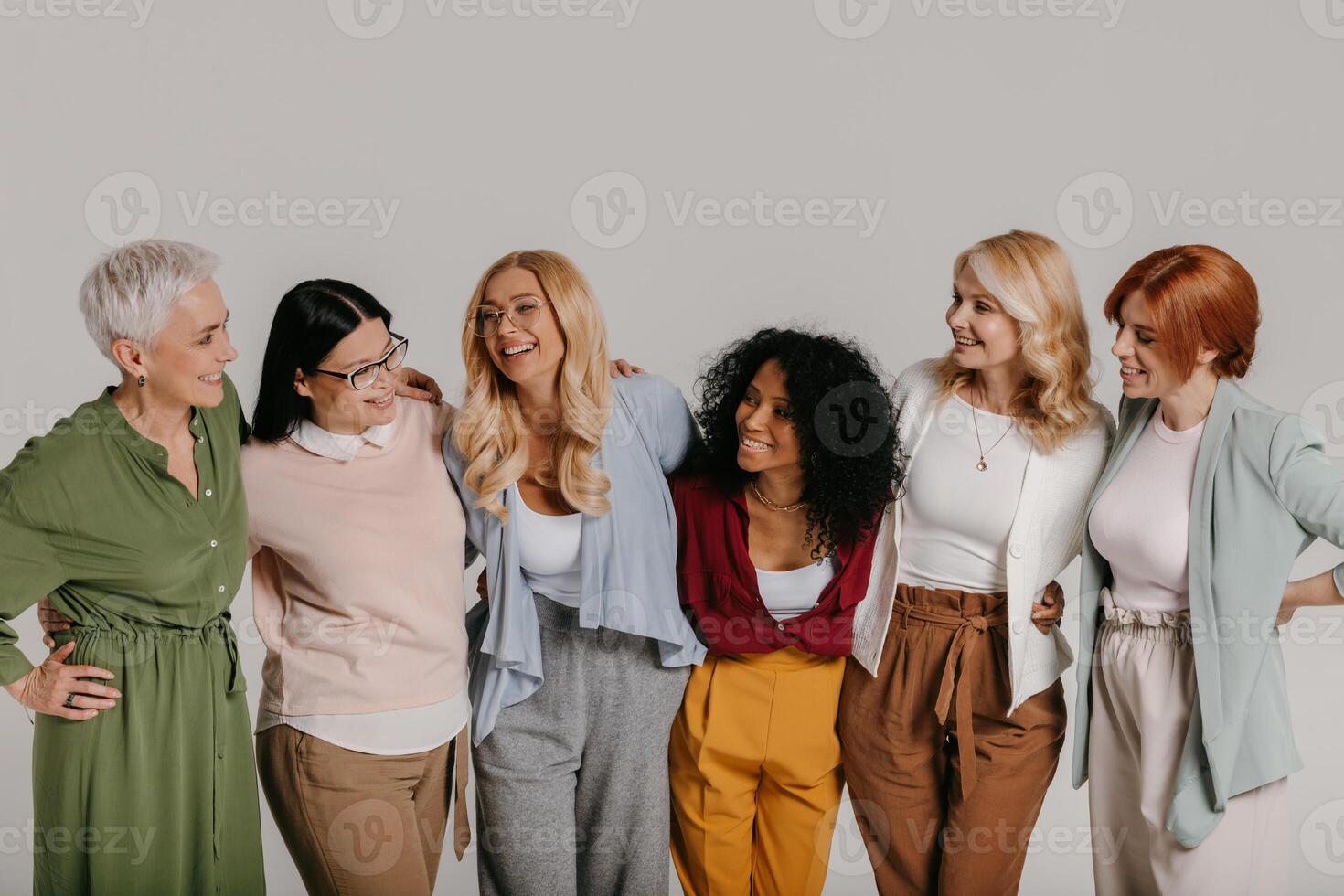 Multi-ethnic group of happy mature women embracing against grey background photo