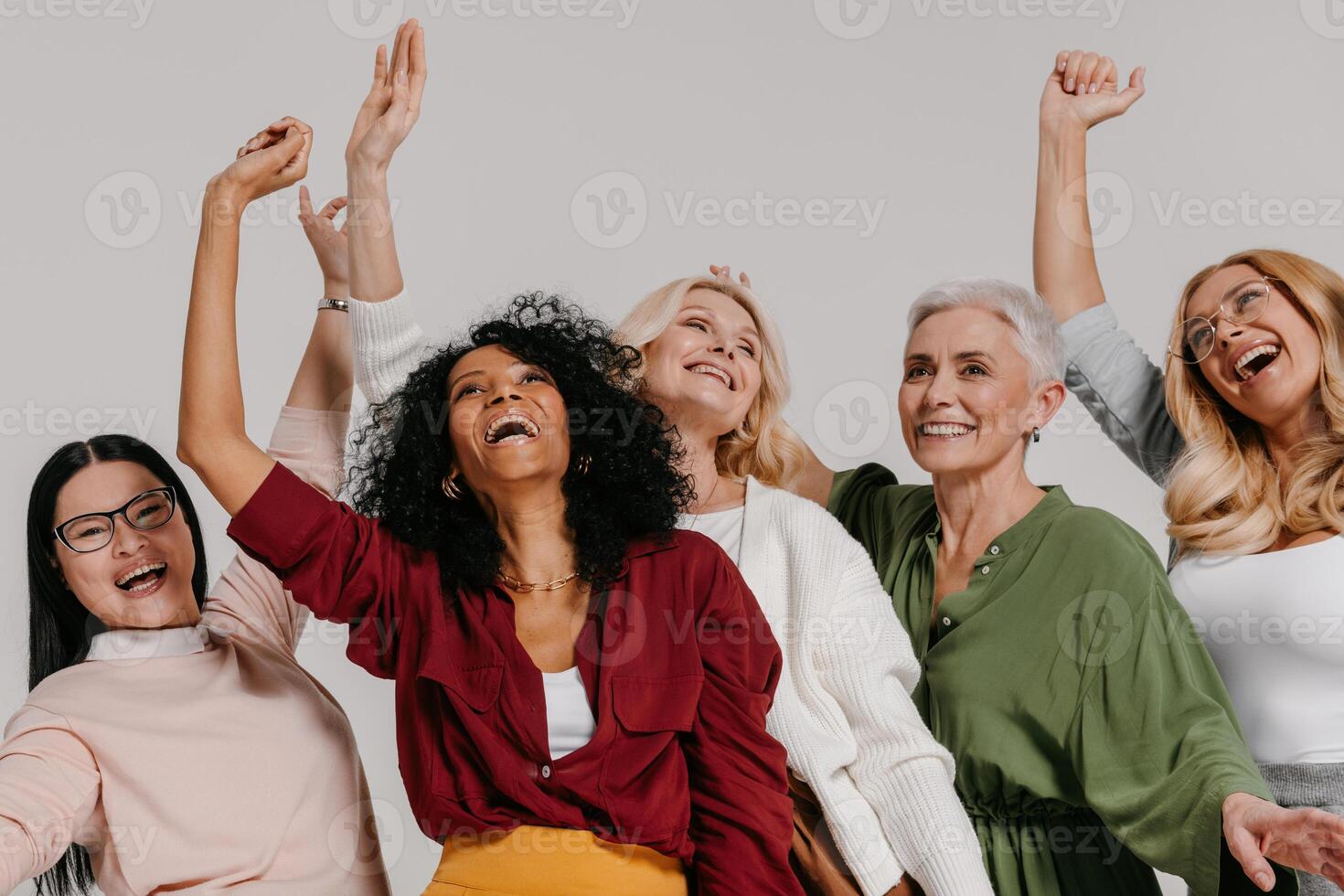 Multi-ethnic group of happy mature women gesturing and smiling against grey background photo