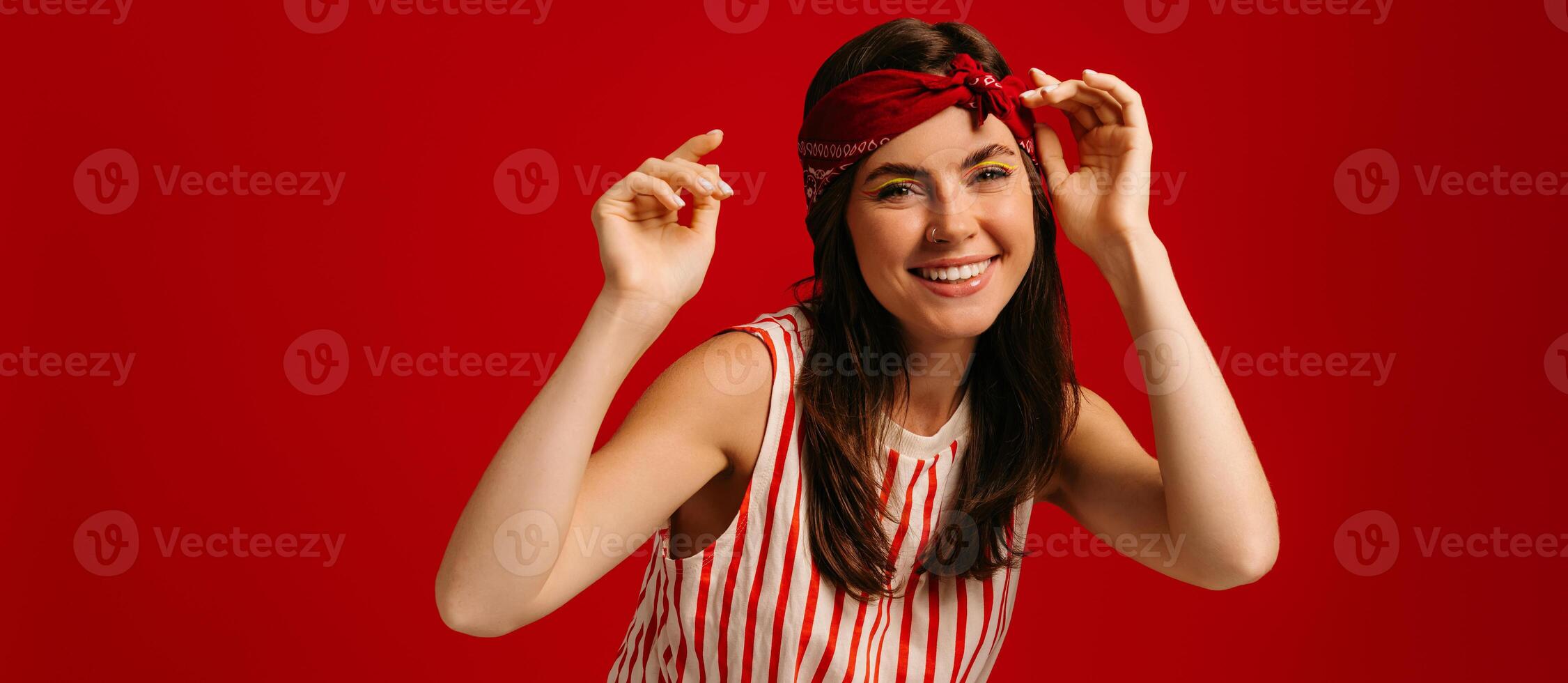 Happy young hipster woman dancing and smiling while standing on red background photo
