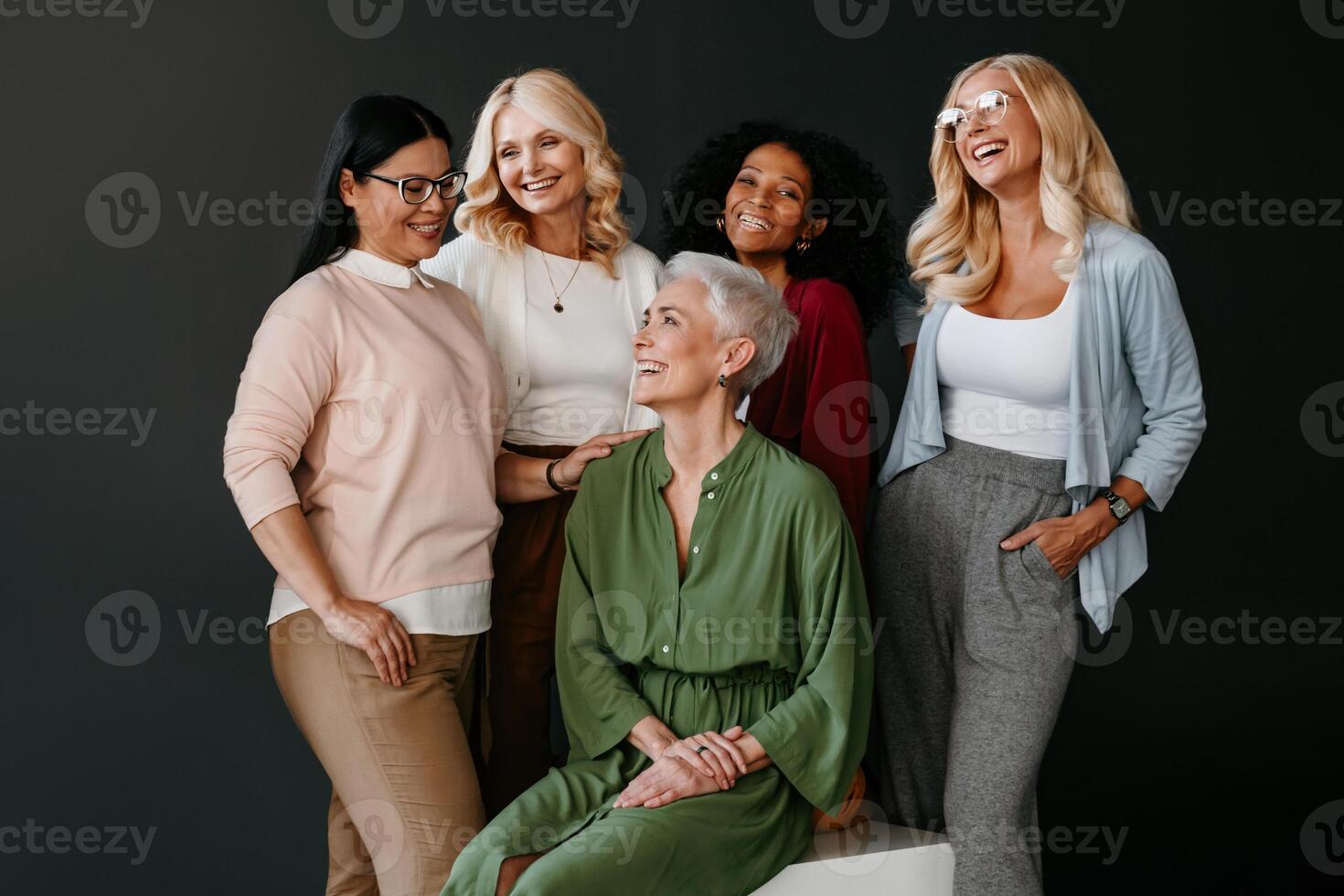 Multi-ethnic group of confident mature women bonding and smiling against black background photo