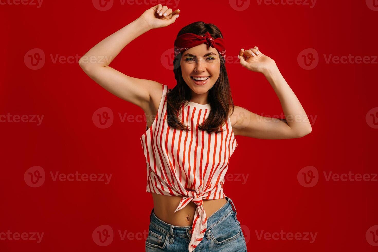 Stylish young hipster woman dancing and smiling while standing on red background photo