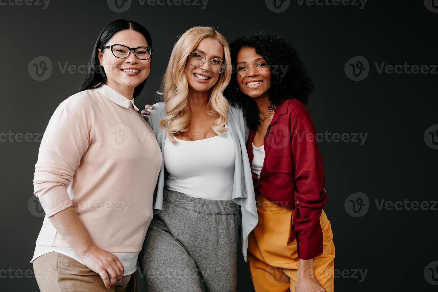 Three happy mature women bonding and smiling against grey background photo