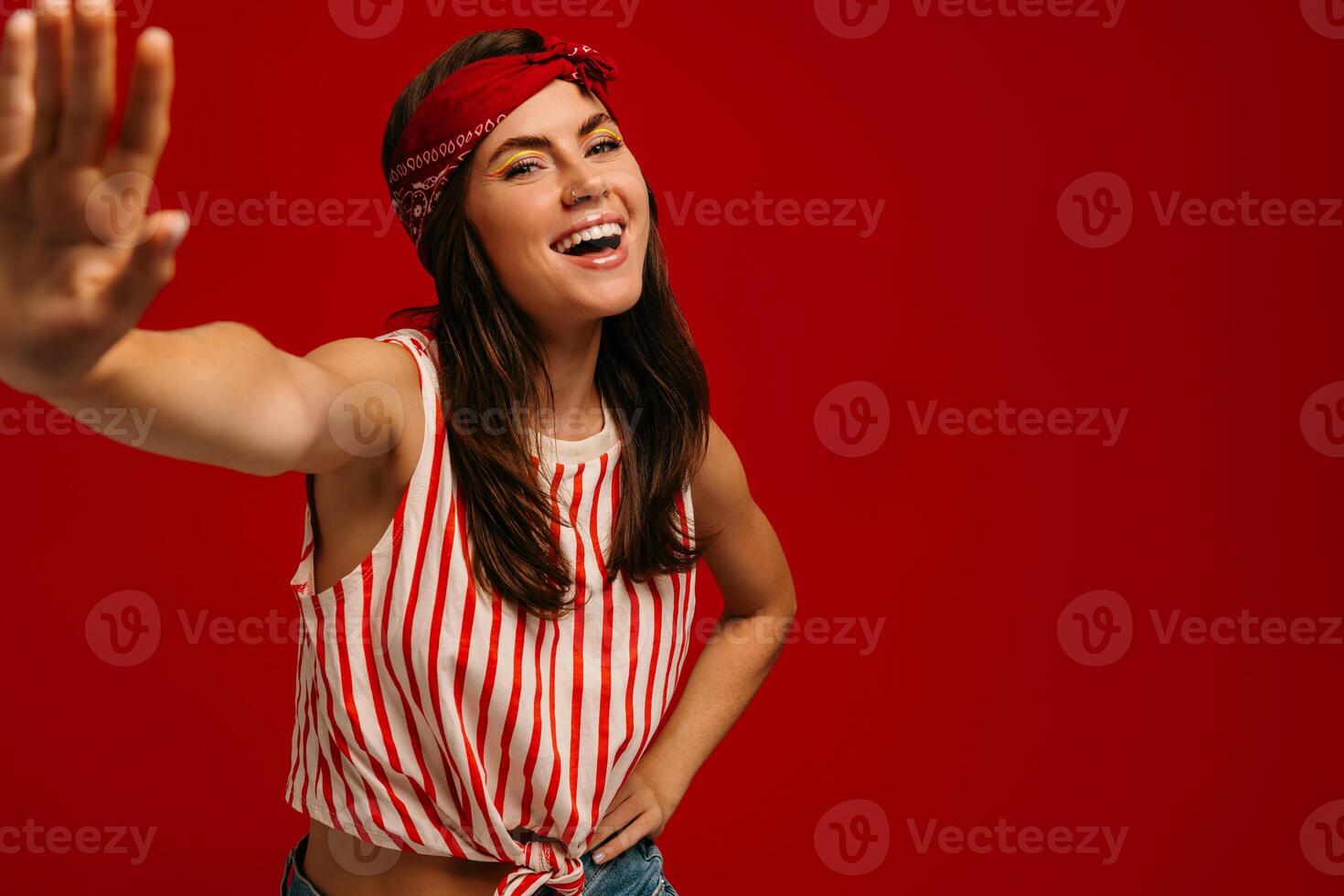 Happy young hipster woman stretching out hand and smiling while standing on red background photo