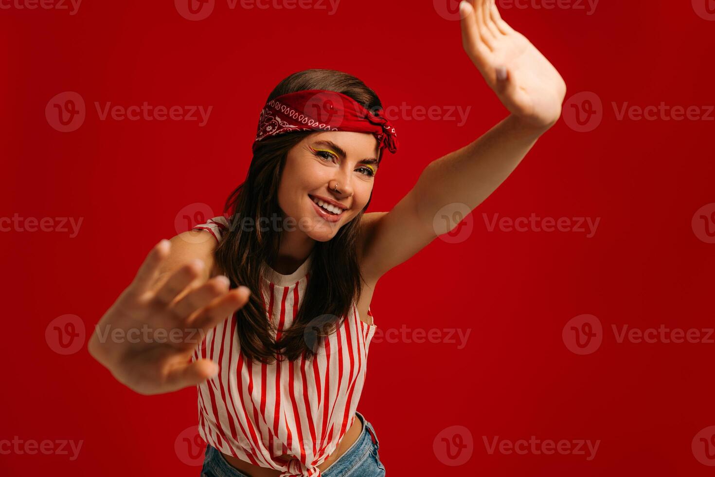 Happy young hipster woman stretching out hands and smiling while standing on red background photo