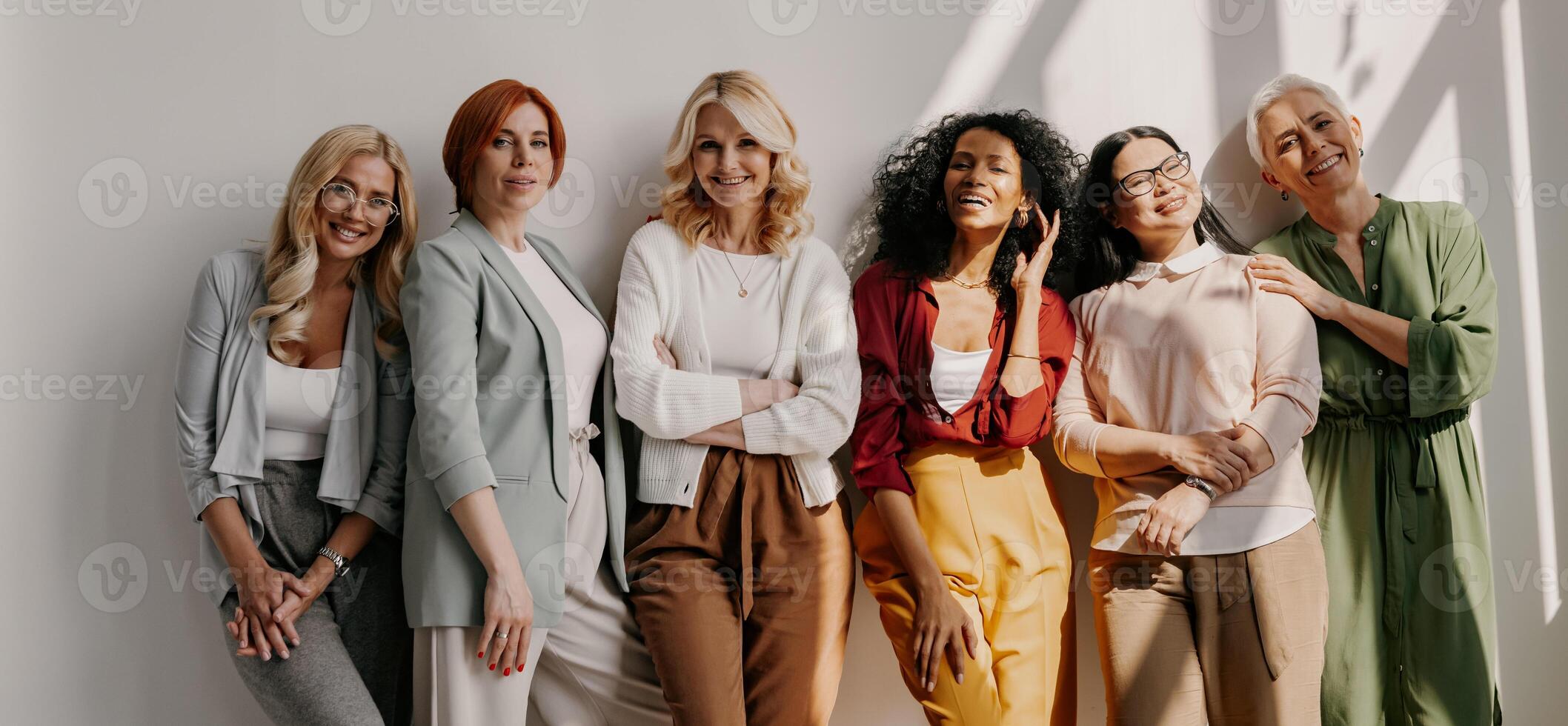 Multi-ethnic group of relaxed mature women bonding and smiling while leaning on the wall photo