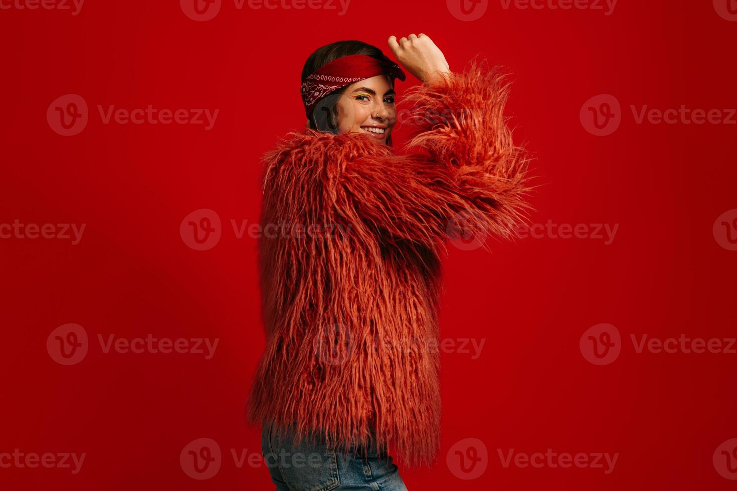 Attractive young hipster woman wearing fluffy coat standing against red background photo
