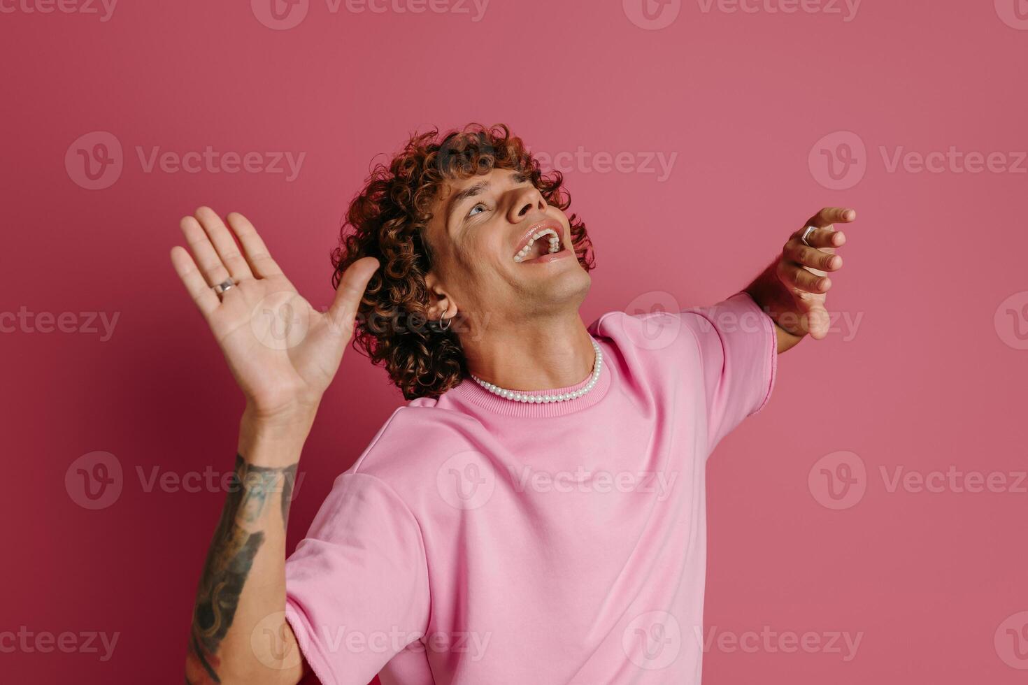 Happy young curly hair man dancing and smiling against pink background photo