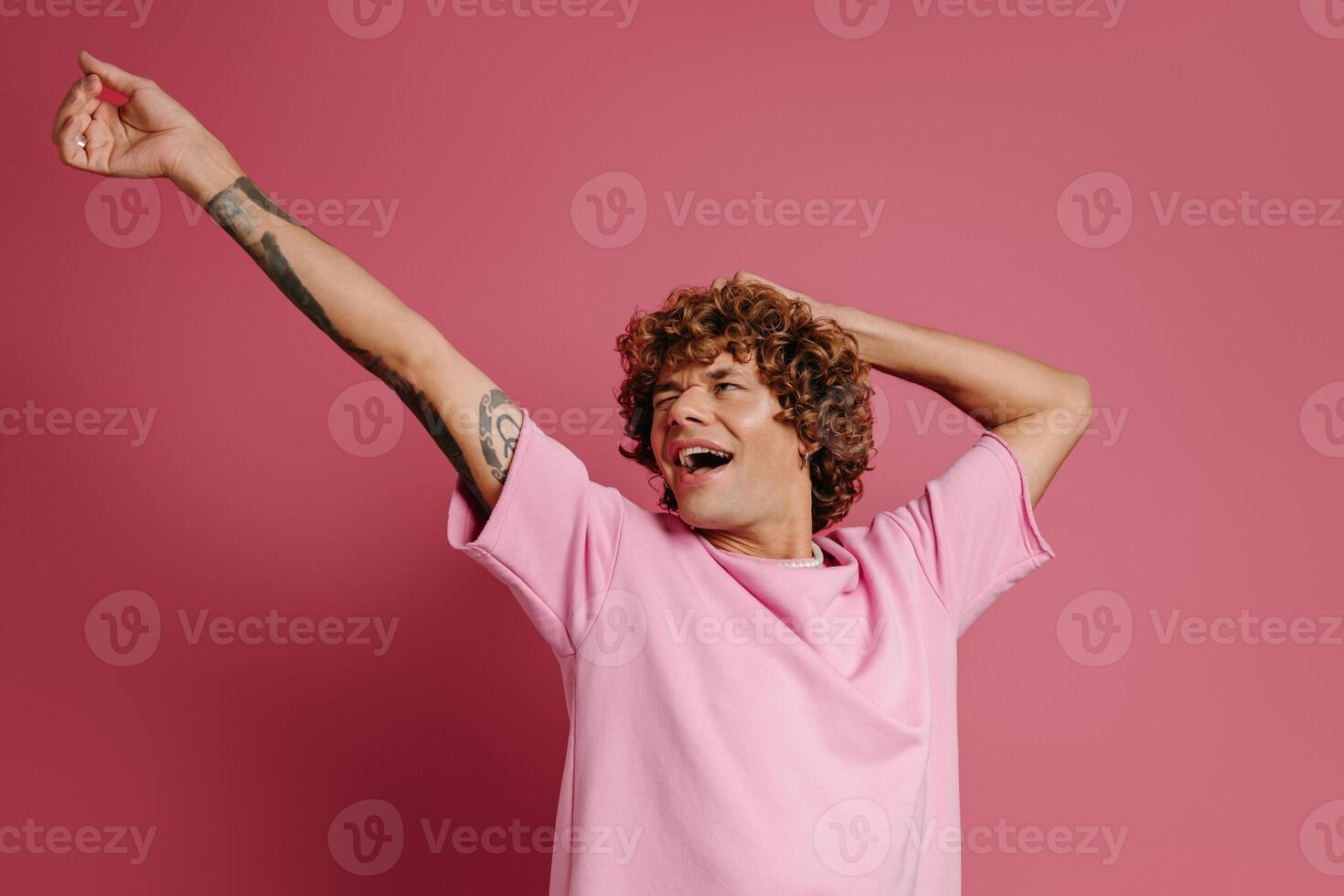 Fashionable young curly hair man gesturing and smiling against pink background photo
