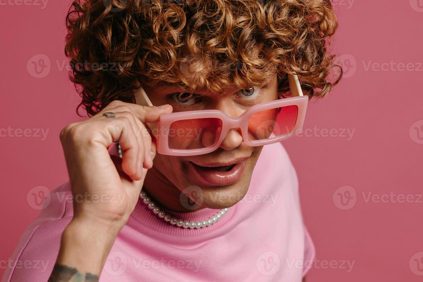 Cool young curly hair man in retro styled eyeglasses looking at camera against pink background photo