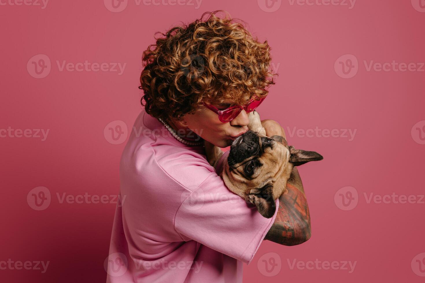 Fashionable young curly hair man petting his cute and smiling on pink background photo