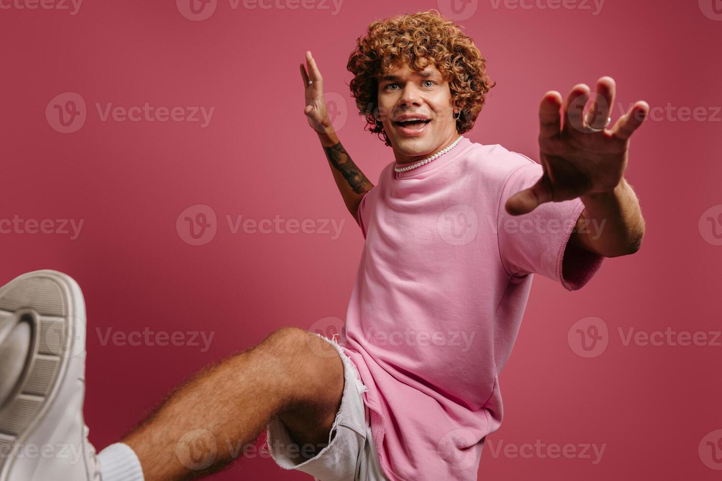 Joyful young curly hair man looking playful while kicking against pink background photo