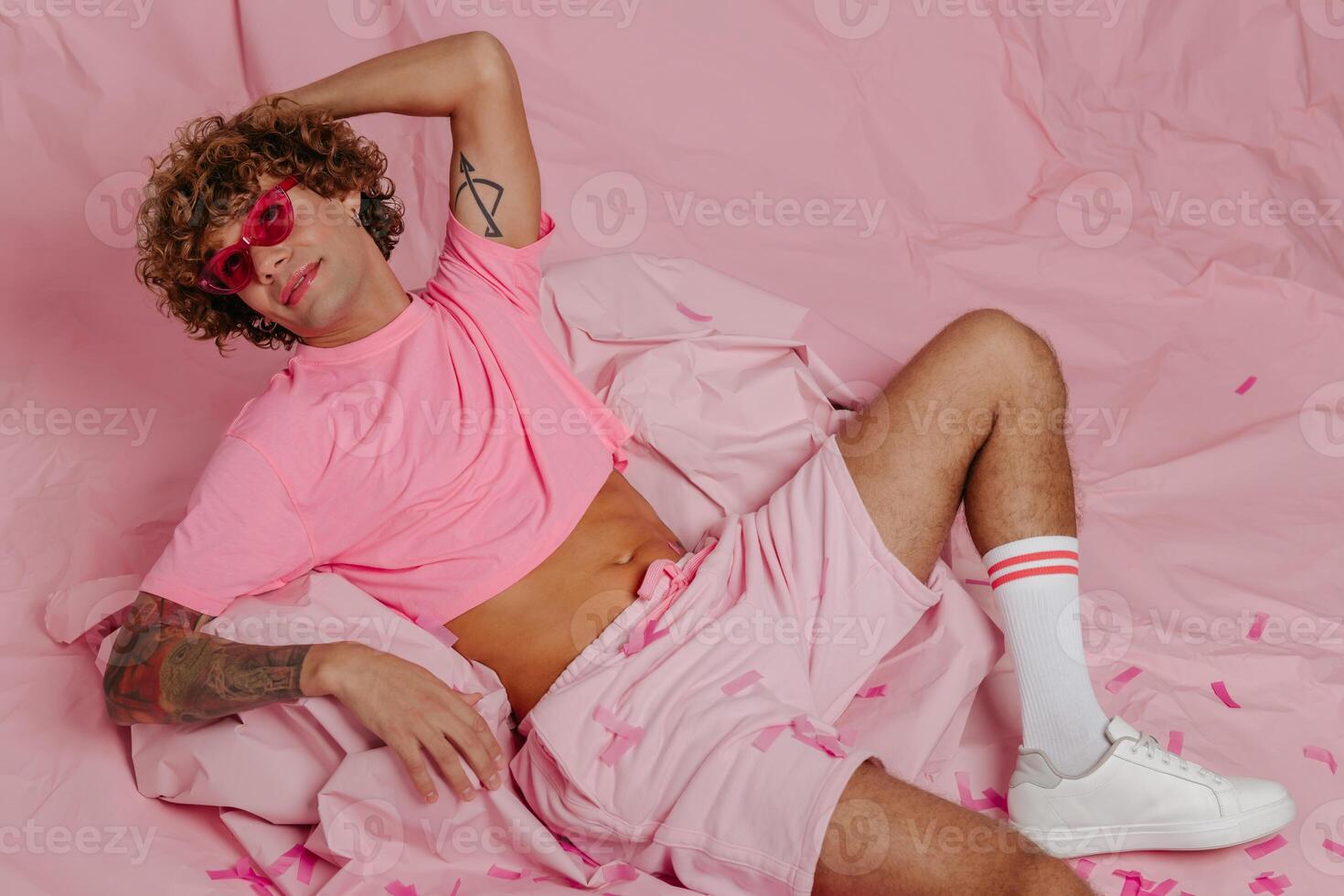 Top view of fashionable young gay man in trendy wear sitting on crumpled pink paper photo