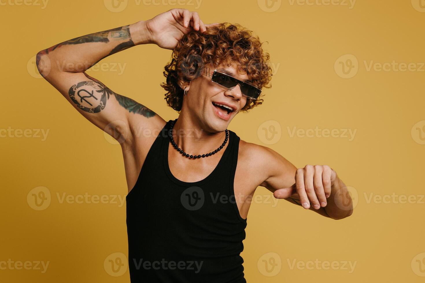 Fashionable curly young man in trendy glasses dancing and smiling against yellow background photo
