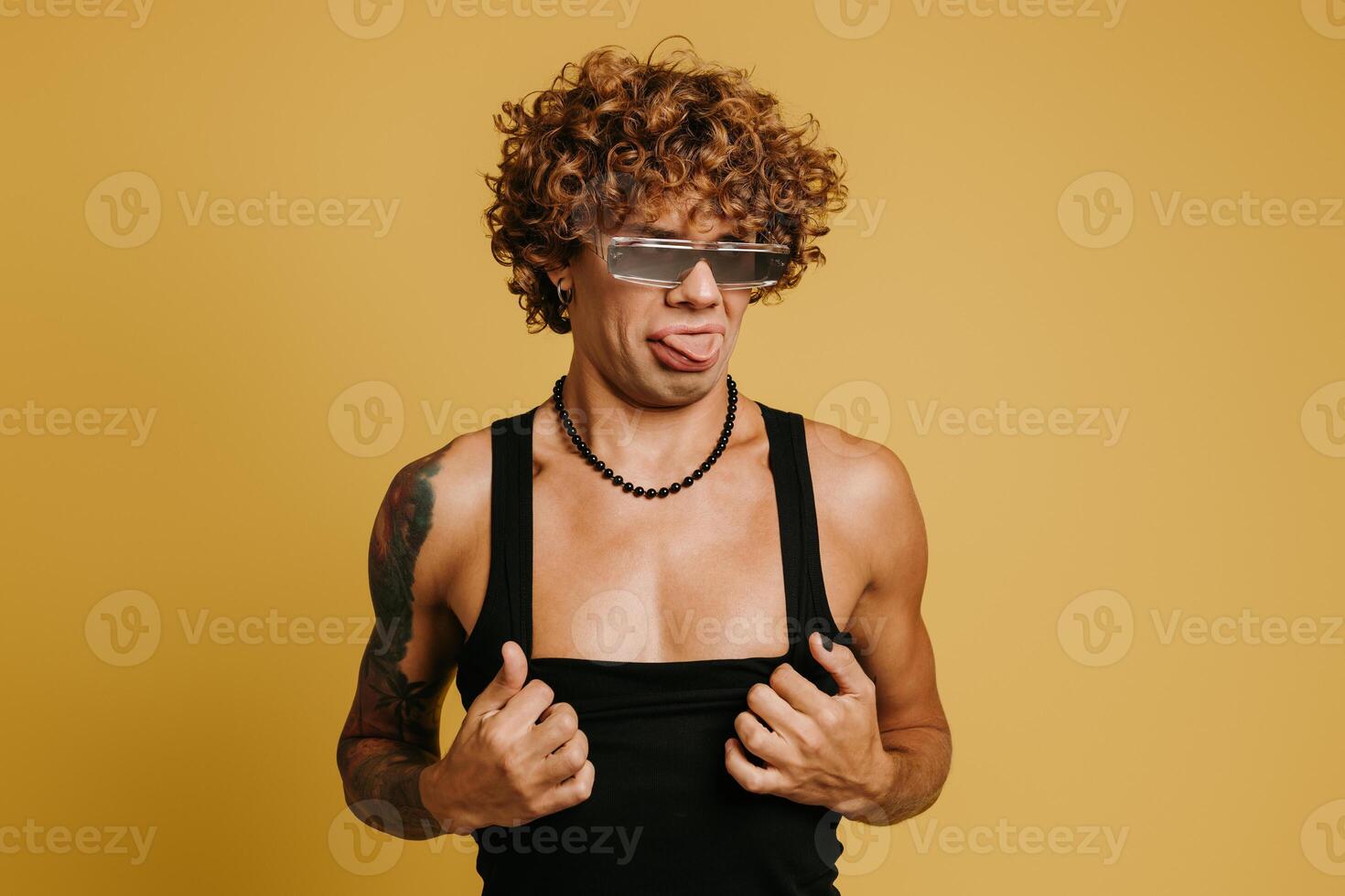 Excited young man in trendy glasses holding hands in hair and smiling against yellow background photo