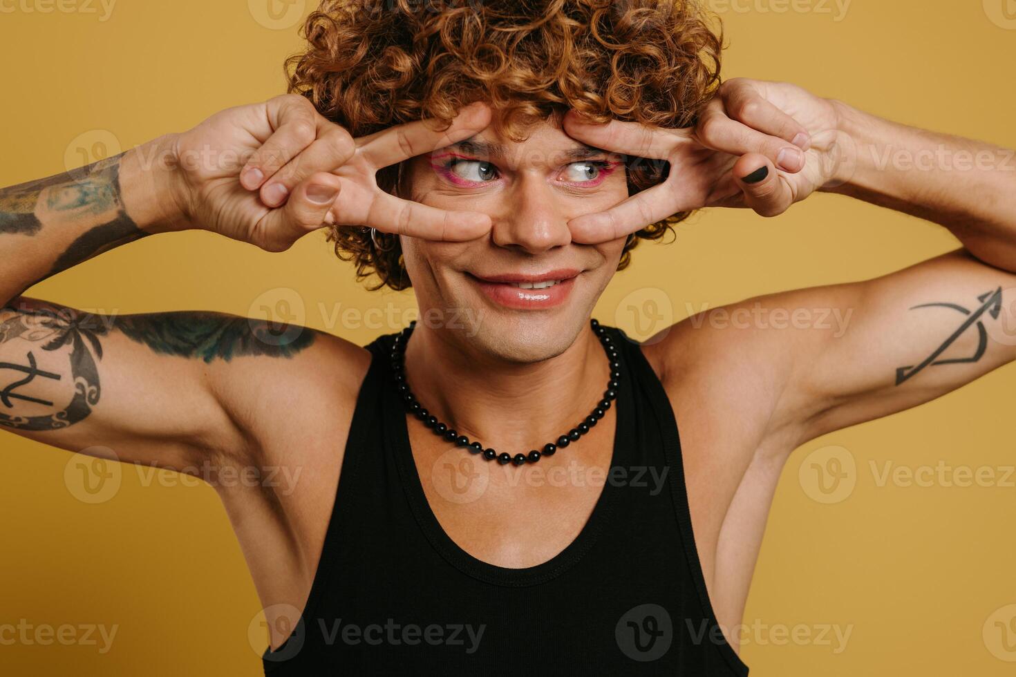 Portrait of playful young gay man showing his face make-up and smiling against yellow background photo
