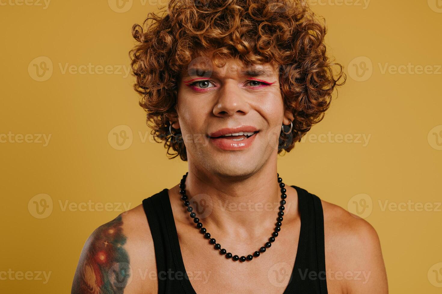 Portrait of handsome young gay man with make-up winking at camera against yellow background photo