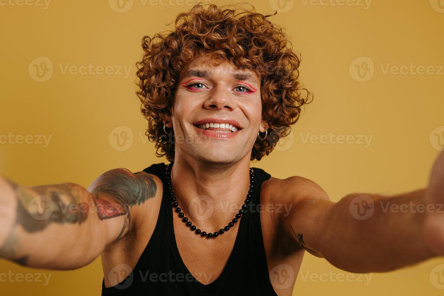 Portrait of handsome young gay man with make-up winking at camera against yellow background photo