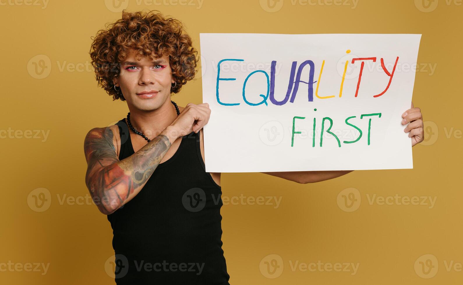 Handsome young gay man with make-up showing colorful banner against yellow background photo