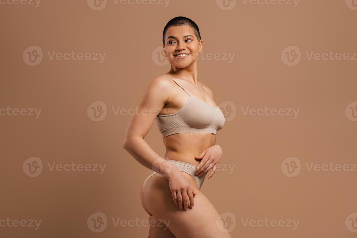 Confident young short hair woman in underwear smiling while standing against grey background photo