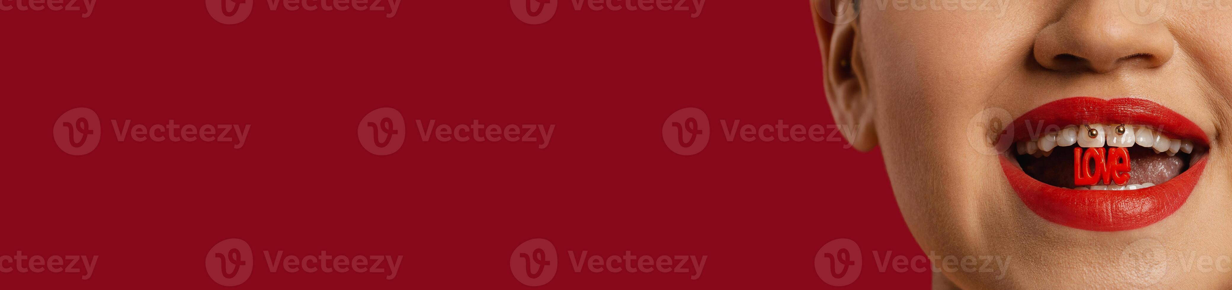 Close-up of unrecognizable woman holding plastic letters in mouth against red background photo