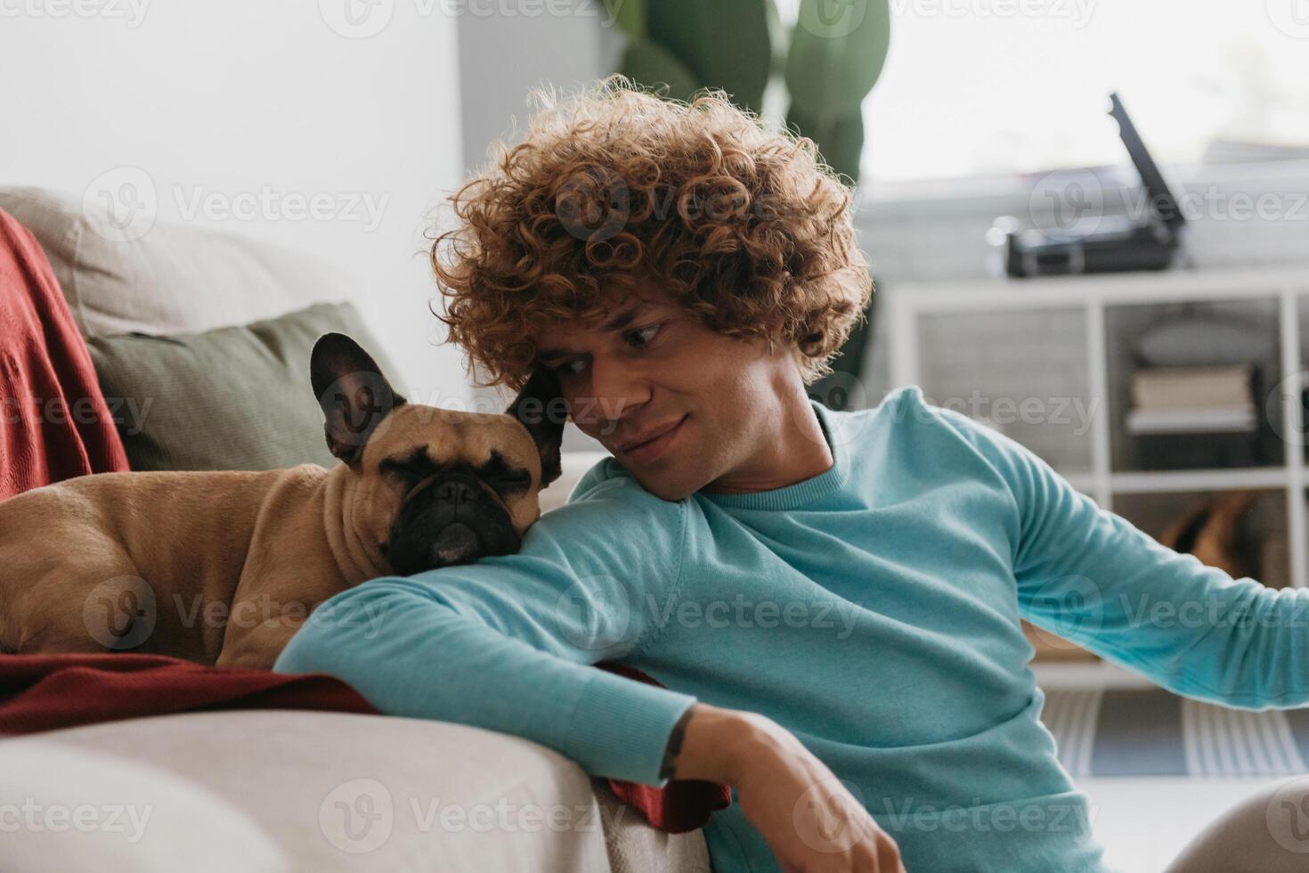 Cute little dog leaning head on shoulder of young handsome man while relaxing at home together photo