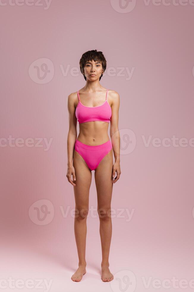 Full length of young short hair woman in underwear standing against colored background photo