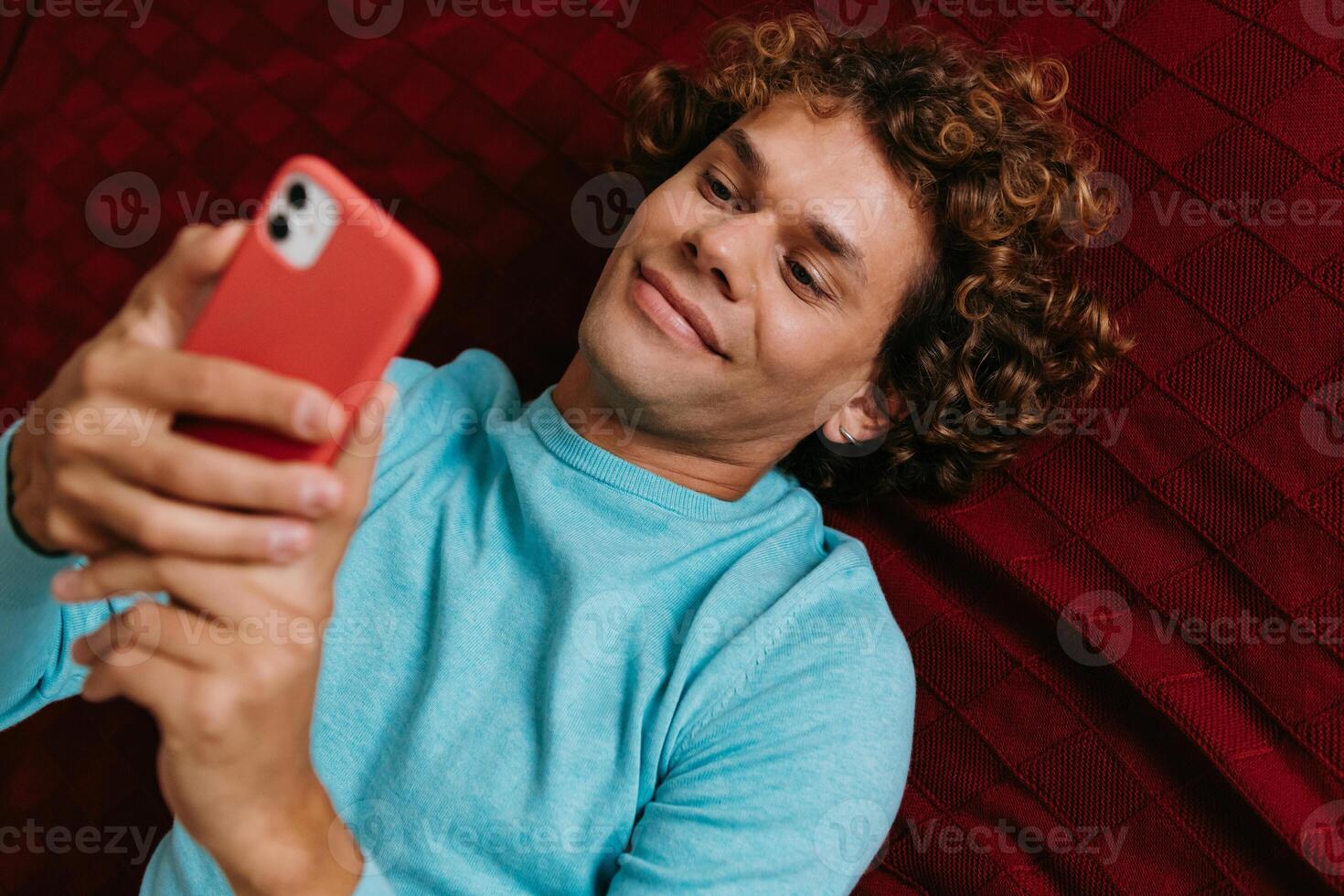 Top view of handsome young man using smart phone and smiling while lying on bed photo