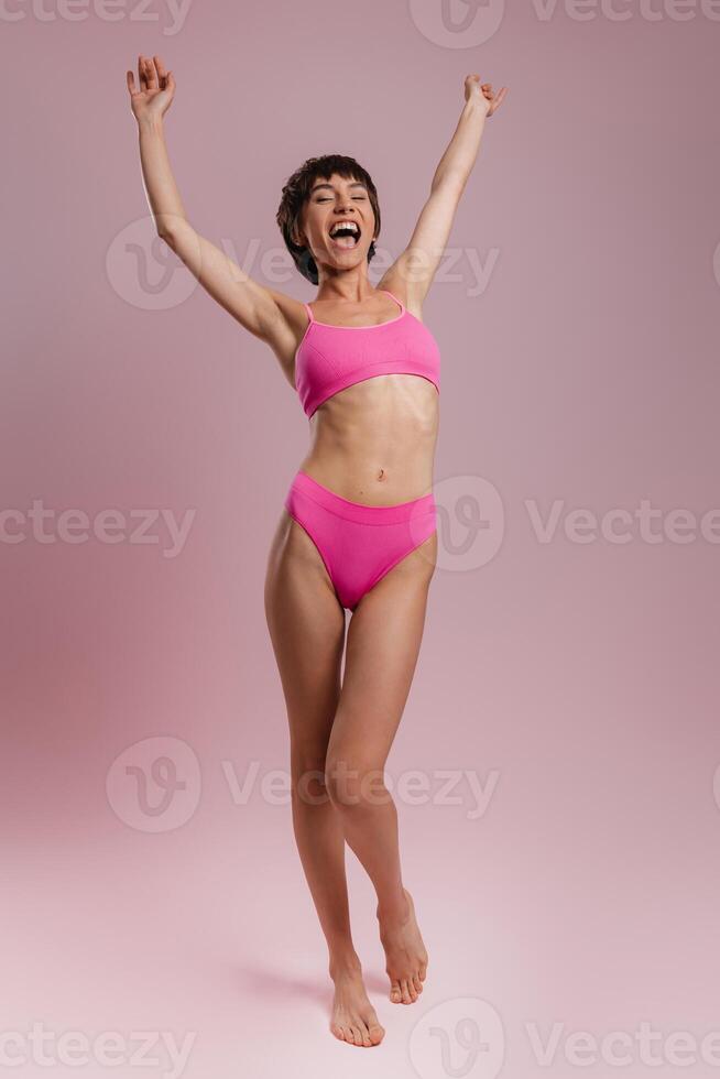 Full length of happy young short hair woman in underwear gesturing against colored background photo