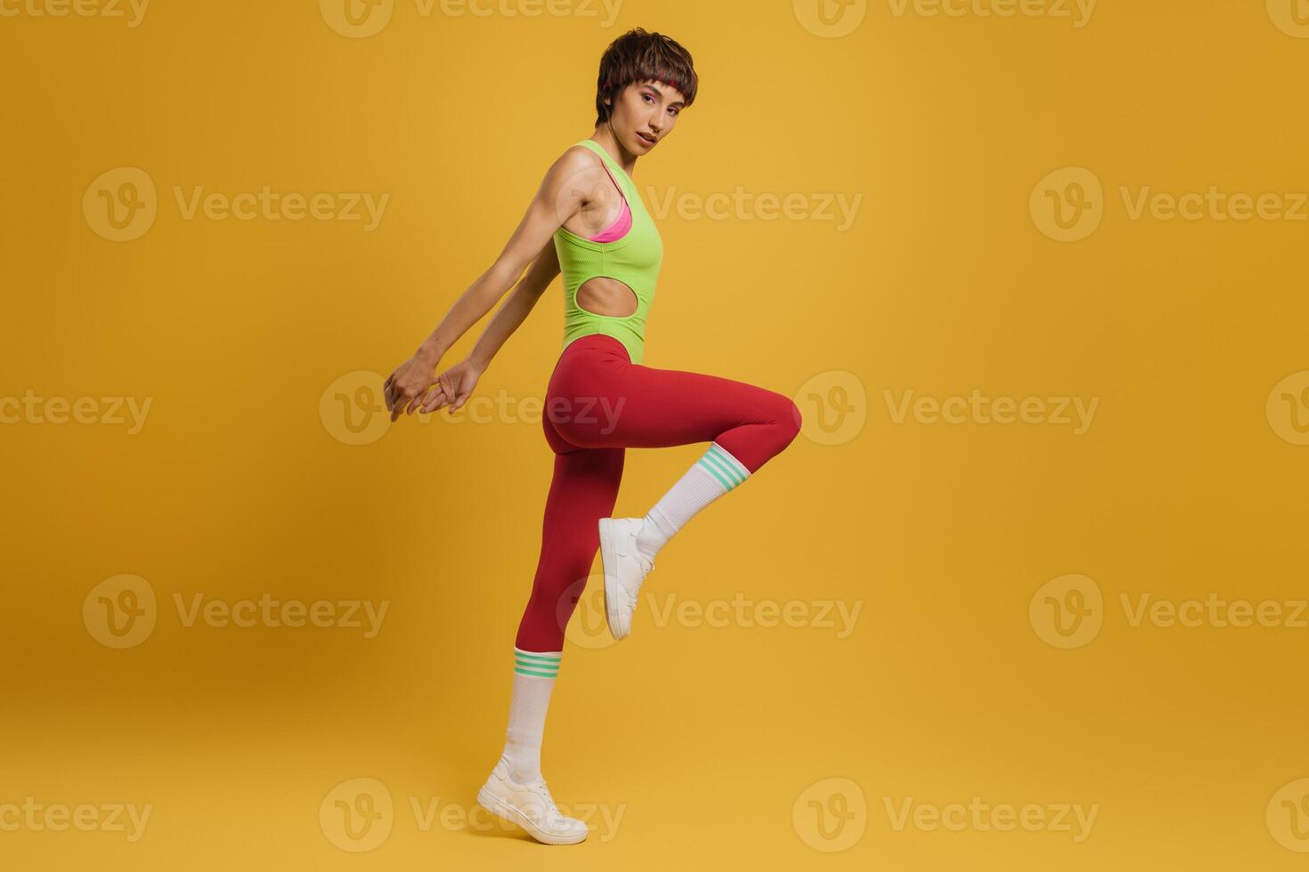 Full length of young fit woman in retro styled sports clothing exercising against yellow background photo