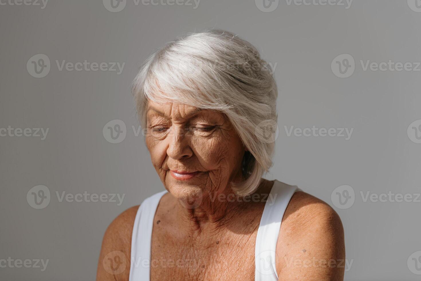 Portrait of confident gray hair senior woman in tank top looking away against background photo