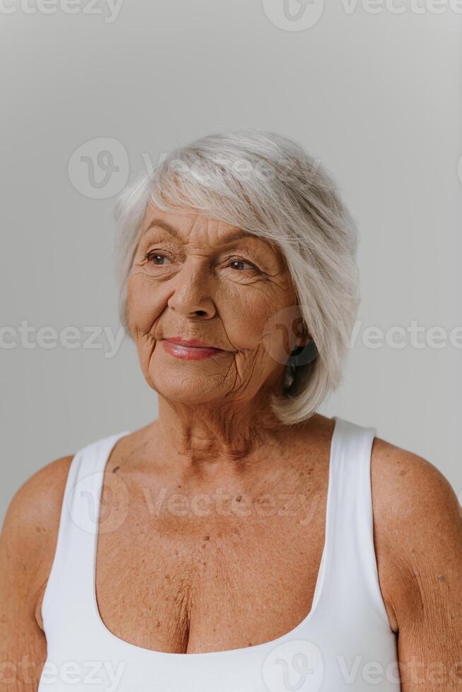 Portrait of confident gray hair senior woman in tank top looking away against background photo