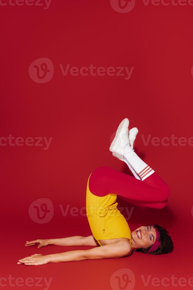 Playful young fit woman in retro styled sportswear exercising against red background photo