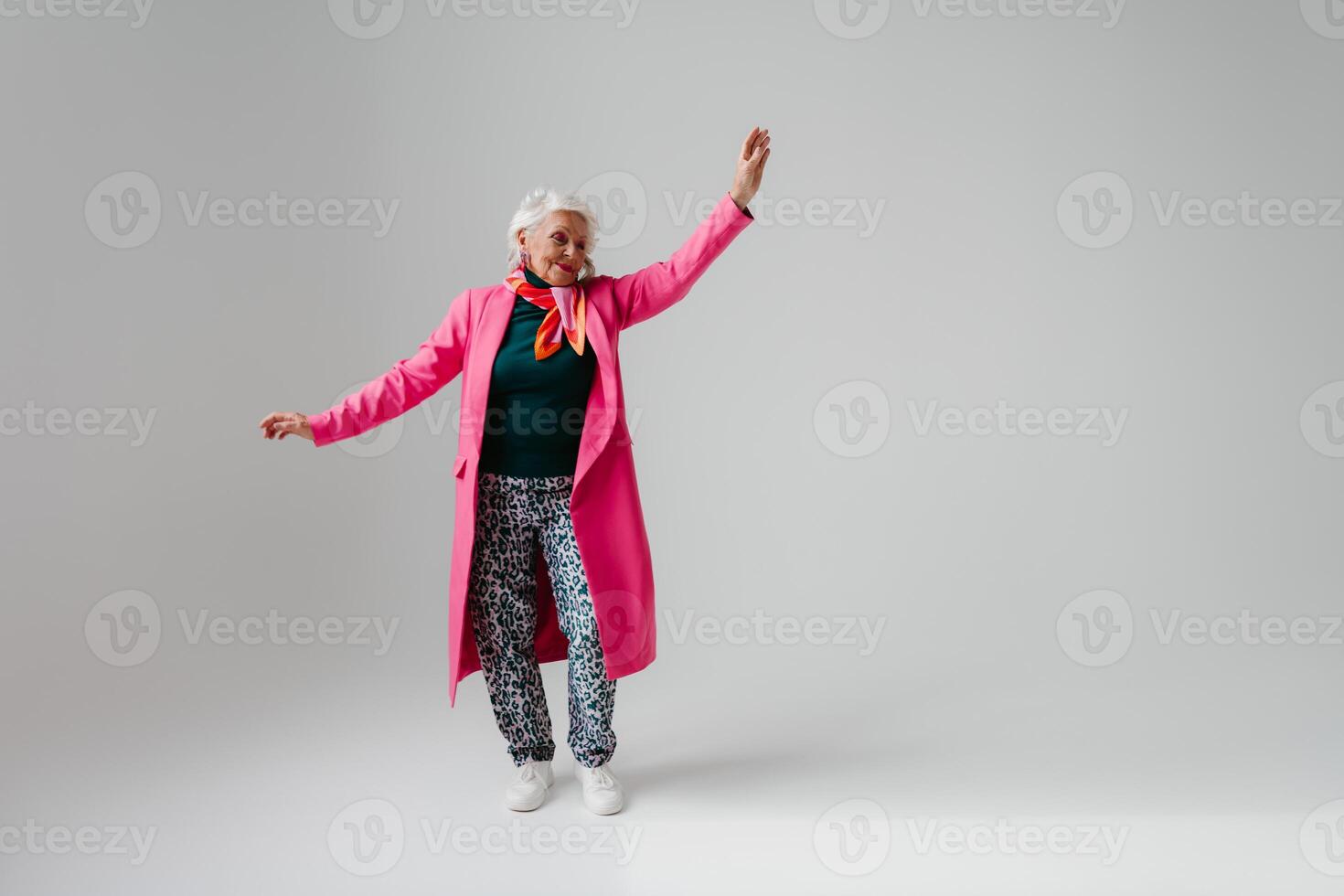 Full length of elegant senior woman in fashionable clothing radiating self-love while dancing on grey background photo