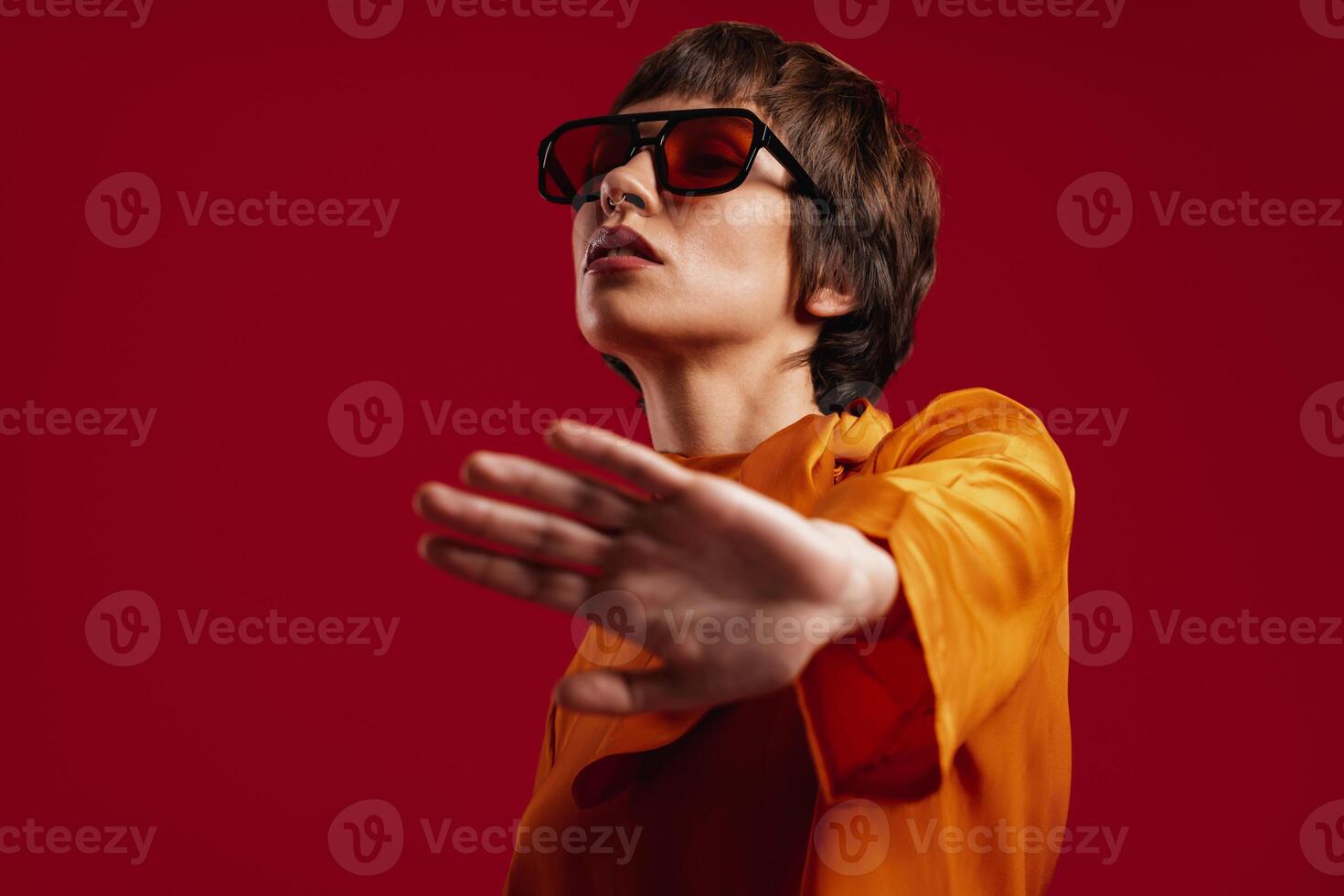 Attractive young short hair woman in trendy glasses stretching out hand against red background photo