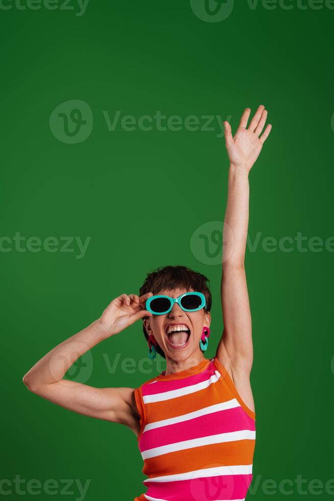 Happy young woman in trendy glasses gesturing while standing against green background photo