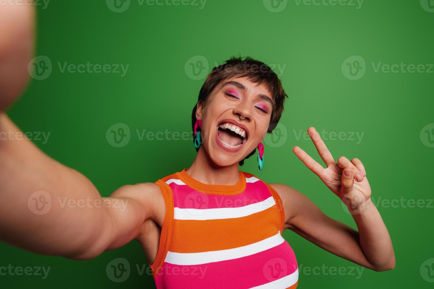 Happy young woman making selfie and gesturing while standing against green background photo