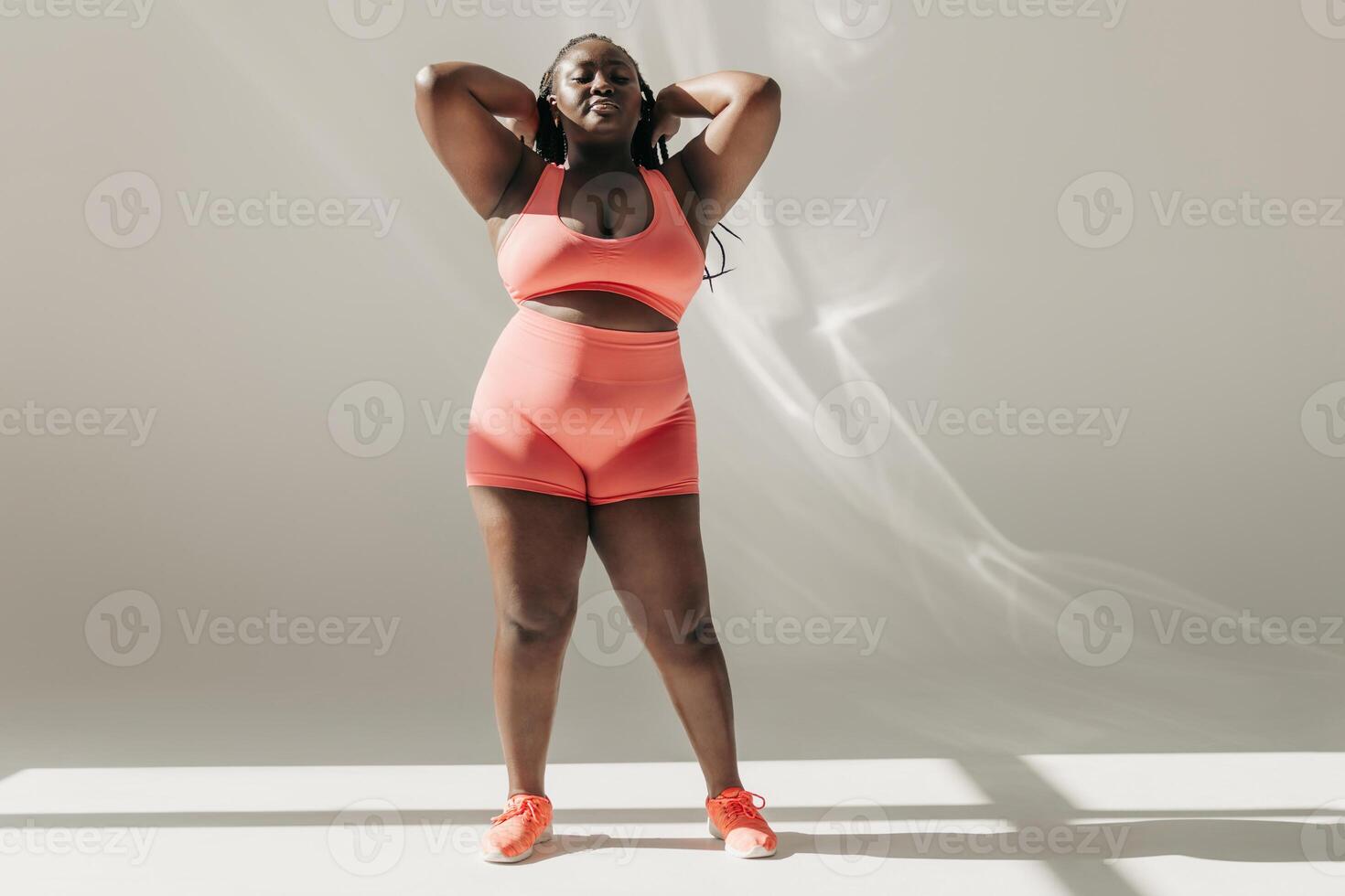 Full length of confident African plus size woman in sportswear adjusting hair while standing in fitness studio photo