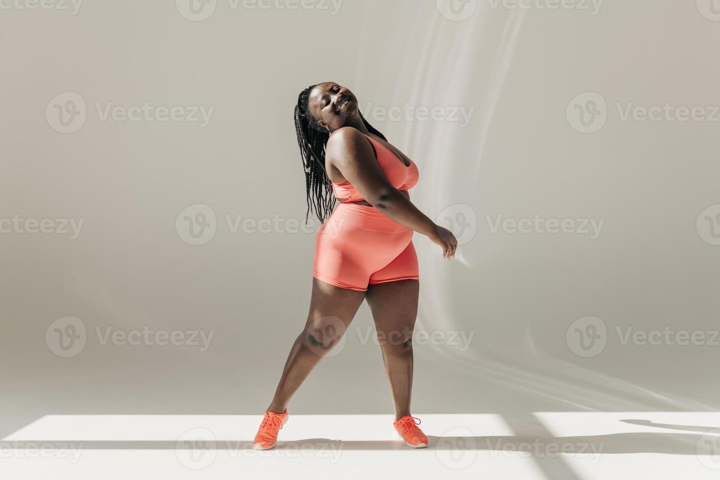 Full length of happy African plus size woman in sportswear radiating self love while standing in fitness studio photo