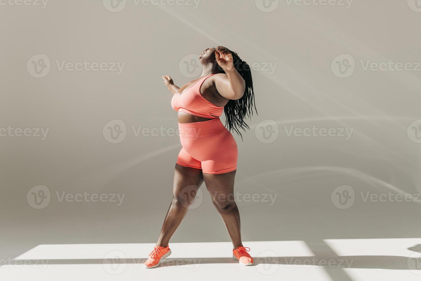Full length of active African plus size woman in sportswear doing stretching exercises in fitness studio photo