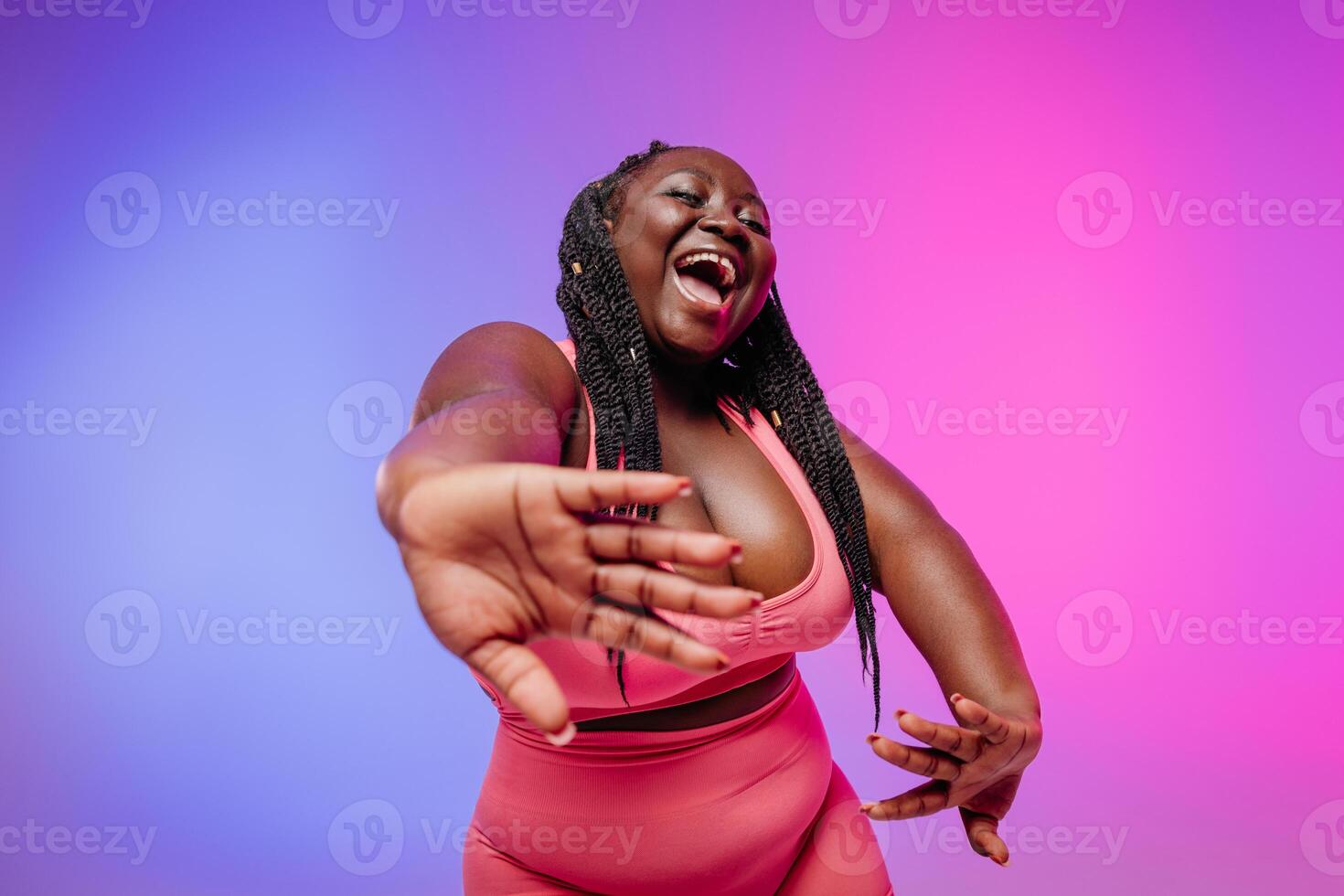 Beautiful African plus size woman in sportswear gesturing and smiling against vibrant background photo